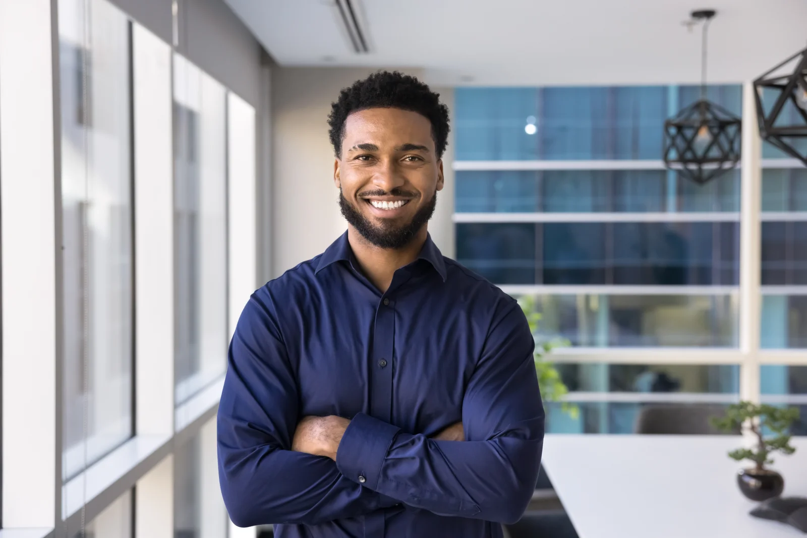 A smiling man in a navy shirt standing by a window